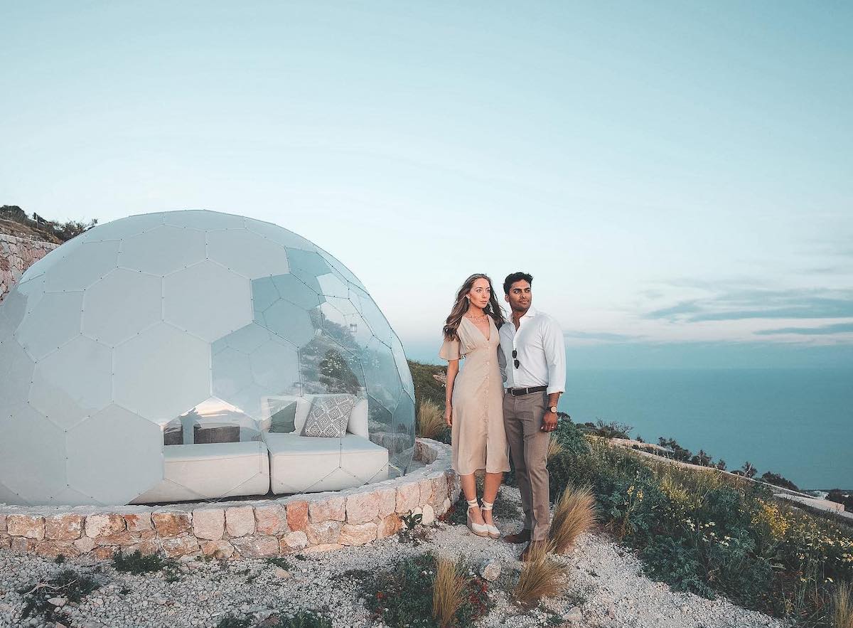 Una coppia in piedi di fronte alla cupola del glamping in riva al mare