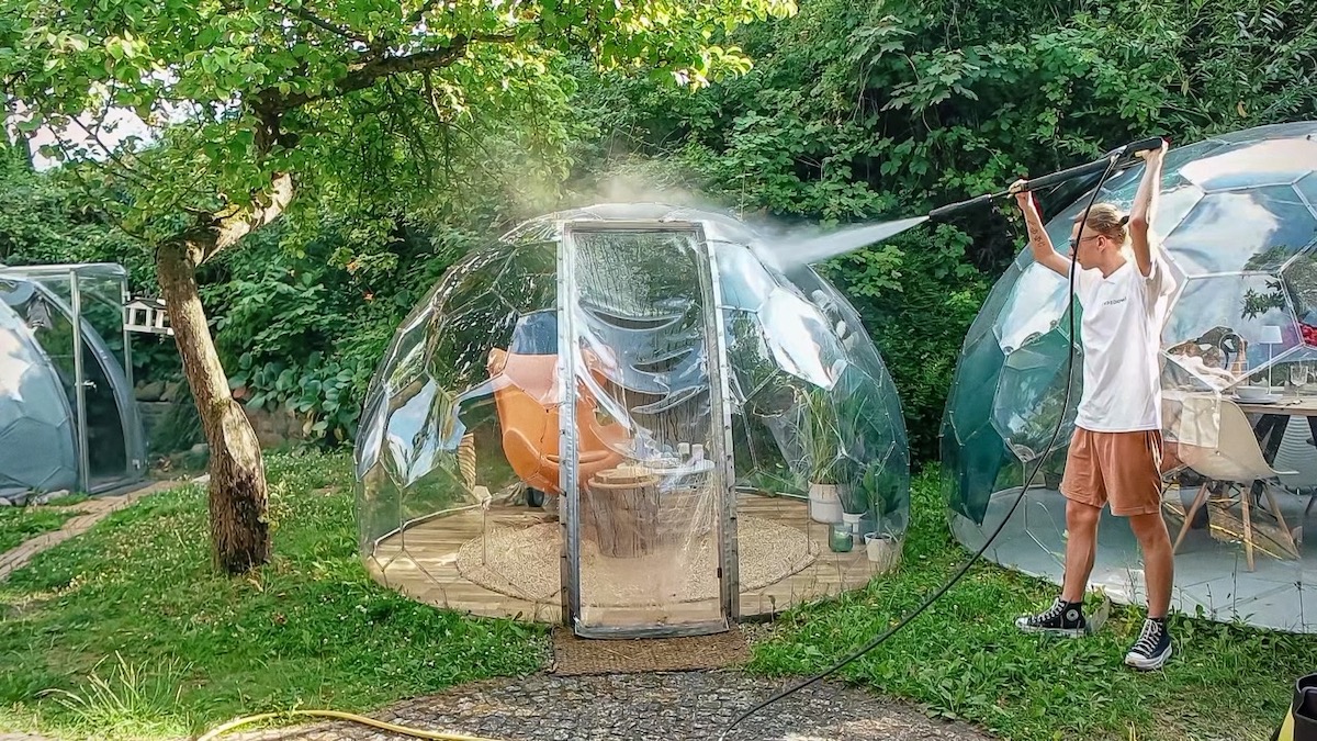 Un uomo che pulisce a fondo una capsula da giardino Hypedome con un'idropulitrice