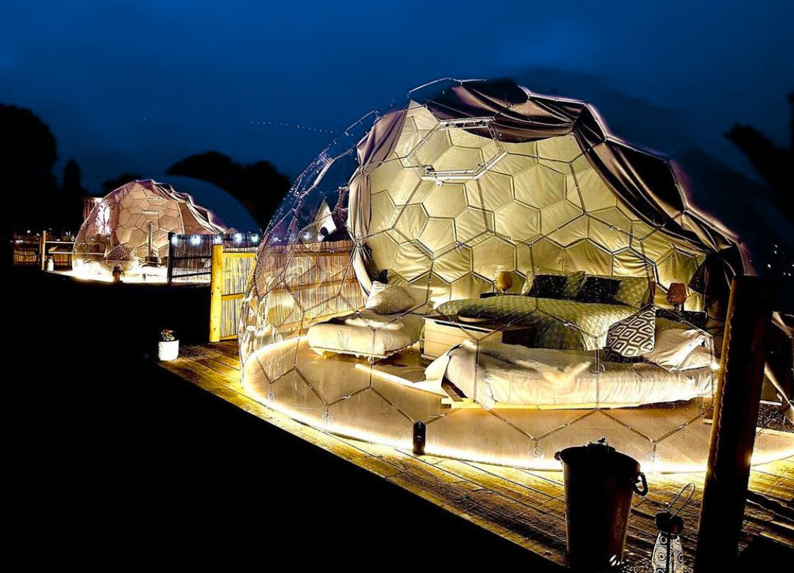 Innenraum einer modernen Glamping-Kuppel mit Bett, Sitzecke und Panoramafenster