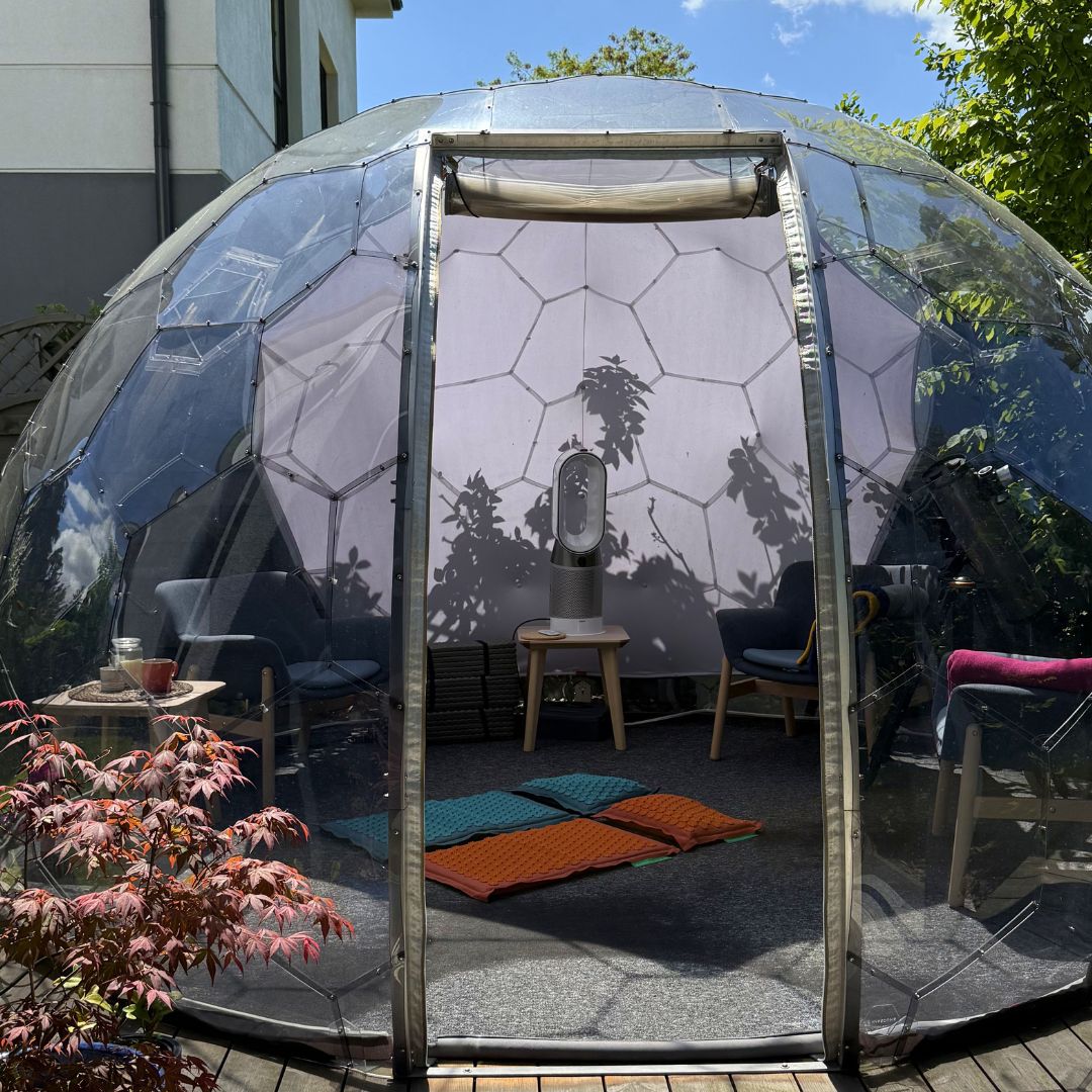 Nahaufnahme einer orangefarbenen Pranamat ECO-Akupressurmatte, hinter der im Garten ein Hypedome zu sehen ist