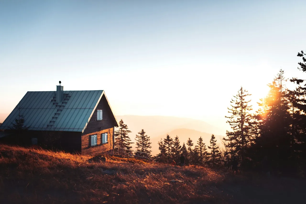 A-frame cabin with illuminated windows and a fire pit in an autumn forest