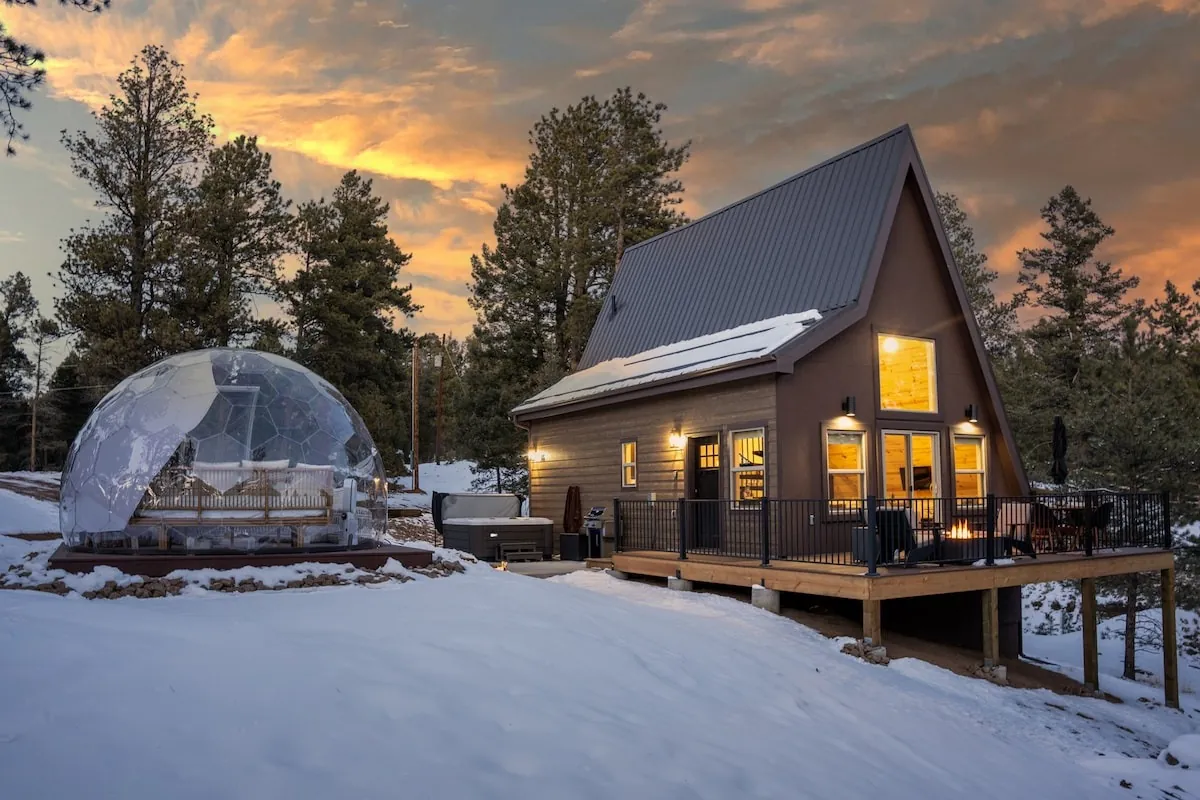 A Hypedome and an A-frame cabin side by side in a snowy landscape at sunset
